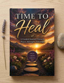 A hardcover book titled 'TIME TO Heal' lies flat on a light wood surface, surrounded by a dried lavender stem on the left and a smooth gray stone on the right. The cover features a scenic landscape of a mountain lake at sunset with a stone path leading into the flowers.