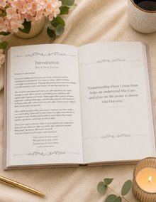 An open book spread showing the Introduction page of a journal or book, styled on a beige fabric surface with pink flowers, a ceramic mug, and a lit candle. Therapeutic journal for women